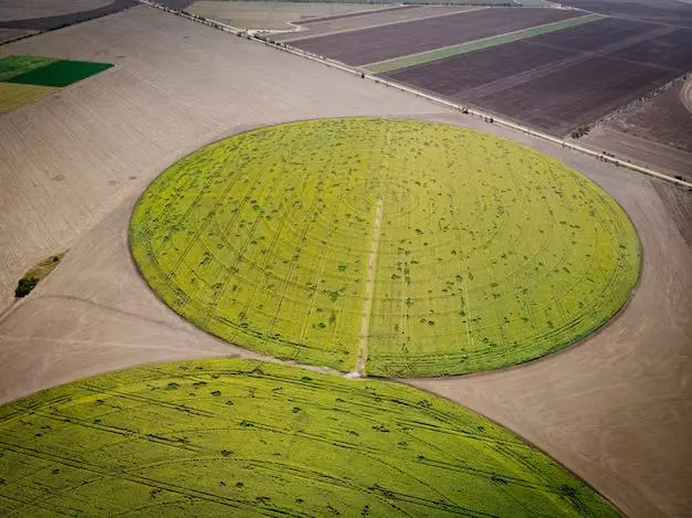 Pivô central visto do alto, formando um círculo verde entre áreas de solo preparado